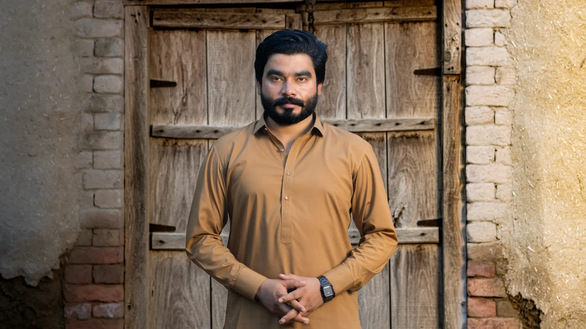 Khizar Omer in a tan kameez standing before an old wooden door