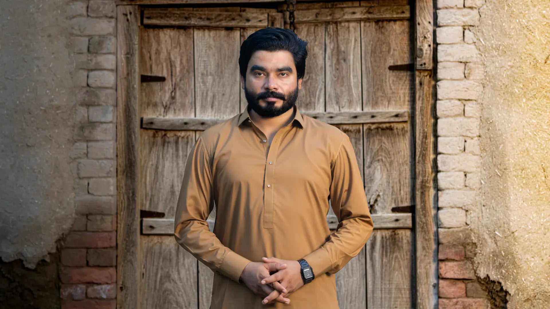 Khizar Omer in a tan kameez standing before an old wooden door